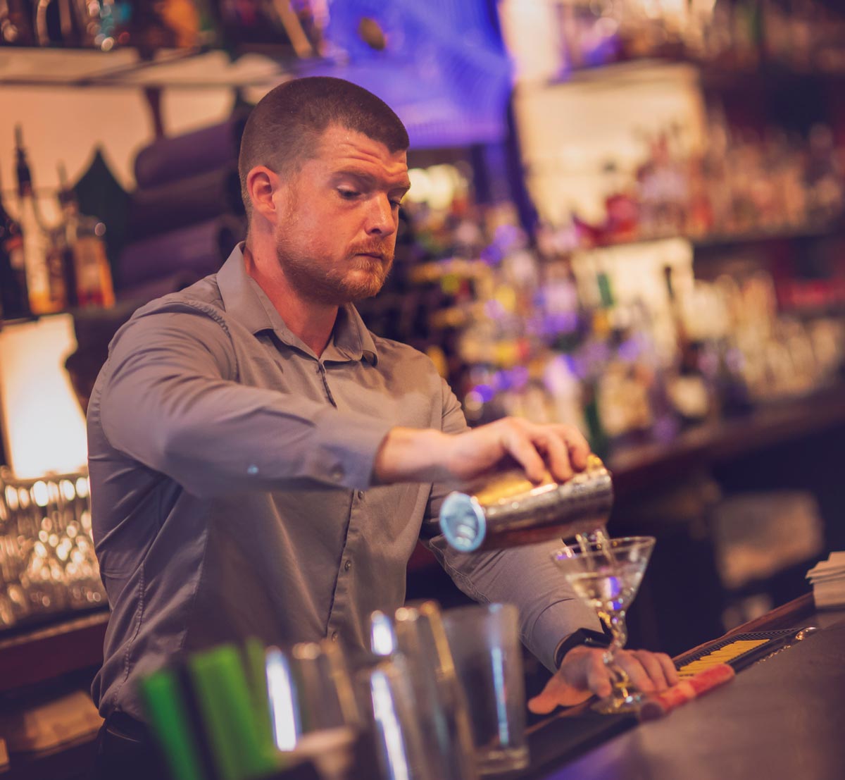 Bartender pouring out a drink into martini glass
