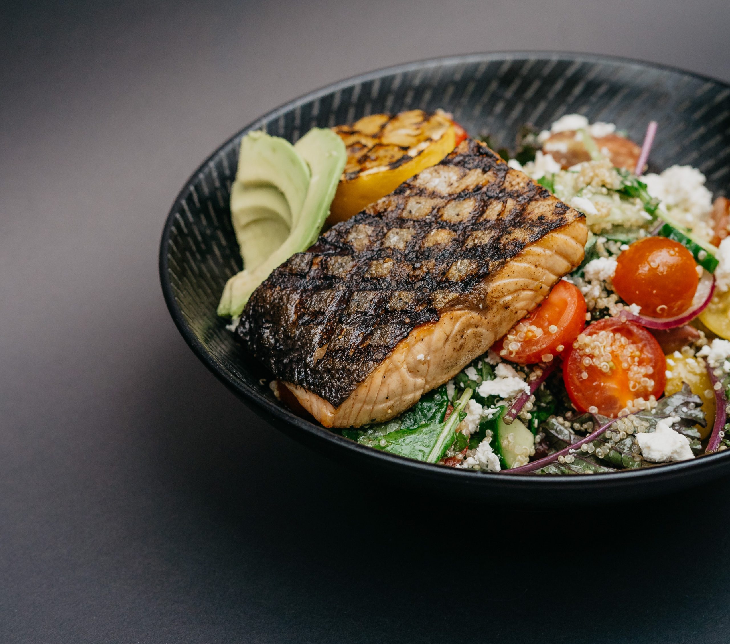 Bowl of grilled veggies topped with a slab of grilled salmon.